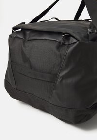 Black waterproof duffel bag with textured fabric panels, adjustable shoulder strap, and zippered top closure on white background.