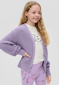 Lichtpaarse gebreide cardigan met losse mouwen en knoopsluiting, gelaagd over een wit t-shirt, gecombineerd met gestreepte lila broek.