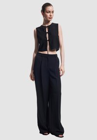 Zwart cropped top met een strikdetail aan de voorkant, gecombineerd met hoge taille, wijde zwart broek. Glad materiaal, minimalistisch design, geen patronen.