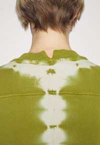 Zielona bluzka w stylu tie-dye z okrągłym dekoltem i małym rozcięciem z tyłu, wykonana z miękkiego materiału o gładkiej fakturze i gradientowym wzorze.