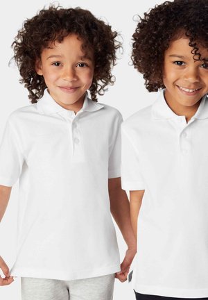 Hvide bomulds polo-shirts med kortærmer, to knapper ved kraven, med struktureret stof. To børn ifører sig dem og smiler.