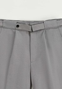 Pantalons gris avec une finition texturée, comprenant une passante de ceinture, une fermeture à bouton unique et des plis sur le devant, présentant un design formel.
