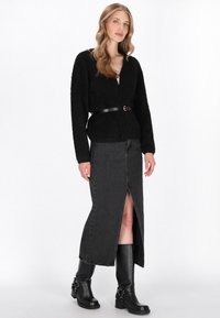 Zwarte pluizige cardigan met een zelfbindende riem, gecombineerd met een zwarte denim rok met een voorkapsluiting, en zwarte leren laarzen met gespen.