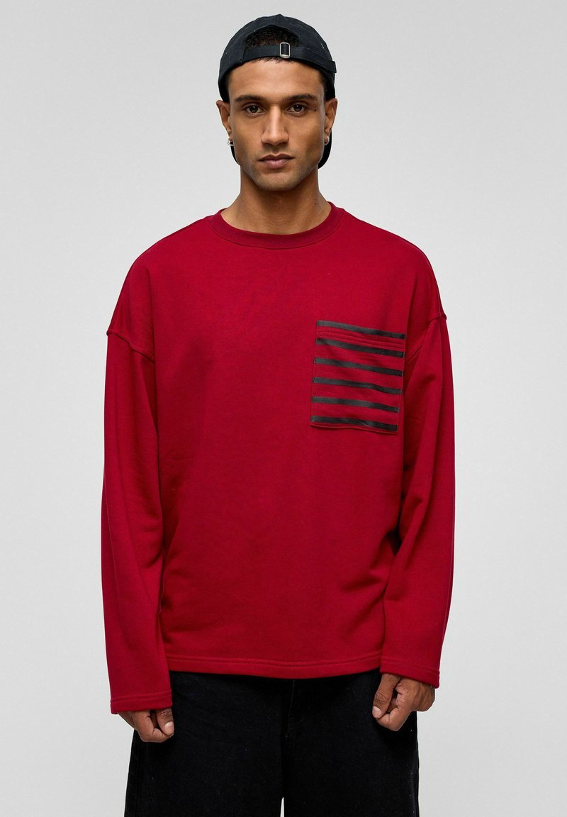 Rode sweatshirt met lange mouwen van zachte stof, voorzien van een zwart gestreepte zak aan de linkerkant, met een ontspannen pasvorm en ronde hals.