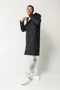 Black waterproof coat with a hood, button-down front, side pockets, and a relaxed fit, paired with gray sweatpants and white sneakers.