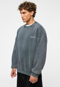 Grijze oversized sweatshirt van katoen, met een ronde hals, ribgebreide manchetten en een klein logo op de borst. Getextureerde stof met een versleten afwerking.