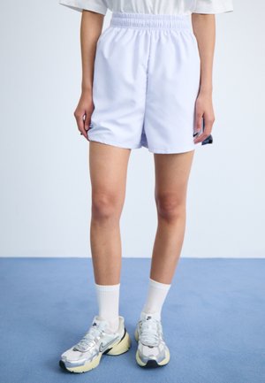 Lys lilla treningsshorts med elastisk midje, brukt med hvite sokker og grå sneakers med svarte detaljer.