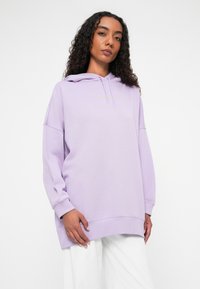 Sweatshirt oversized lavanda com cordão, punhos e bainha canelados. Apresenta um pequeno logotipo dourado no peito. Tecido macio e ajuste descontraído.