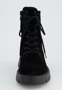 Botte chelsea en suède noire avec bout rond, avant à lacets et semelle en caoutchouc épaisse. Présente des œillets en métal et une tige texturée.