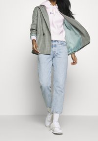 Blazer de cuadros gris de doble botonadura sobre una sudadera rosa, combinado con jeans de pierna recta azul claro y zapatillas deportivas blancas.