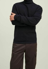 Donkerblauwe geribde coltrui met lange mouwen, gecombineerd met donkere cargobroeken met zijzakken en een gladdere stofstructuur.