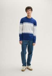 Blau- und graustriped Strickpullover mit langen Ärmeln und Rundhalsausschnitt. Getragen mit blauen Denim-Jeans und beigen Sneakers.
