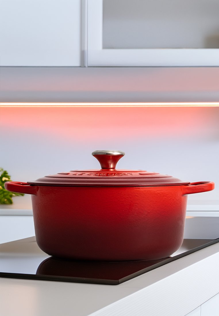 Roter gusseiserner Dutch Oven mit strukturiertem Finish, runder Form und Metallknopf auf dem Deckel, auf einer glatten schwarzen Arbeitsplatte präsentiert.