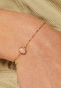 Gold chain bracelet featuring an oval pink stone, finely detailed metalwork, worn on a wrist with a light skin tone.