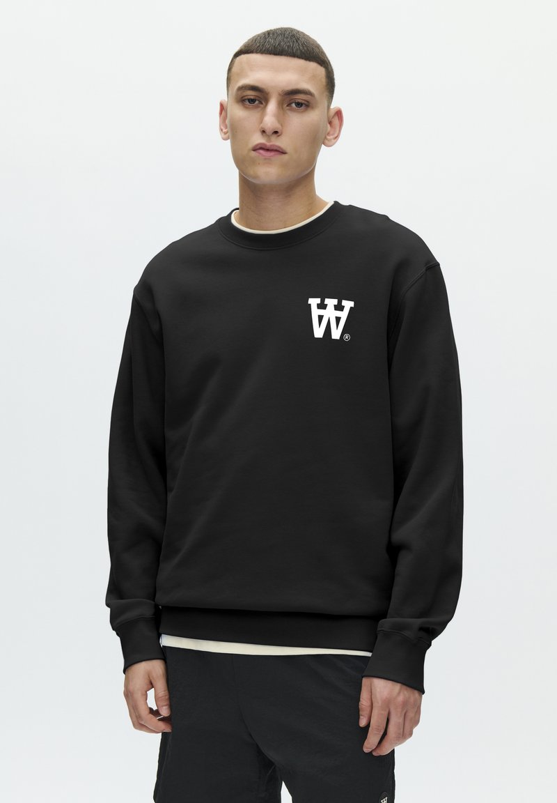 Sweat-shirt noir avec encolure ronde, manches longues et un logo blanc sur la poitrine. Confectionné en tissu doux avec une coupe décontractée.