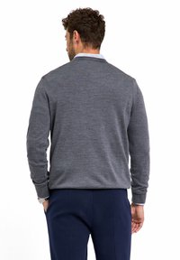 Maglione grigio con un motivo testurizzato, collo rotondo e maniche lunghe, abbinato a pantaloni blu scuro. Dettaglio sulle rifiniture visibili.