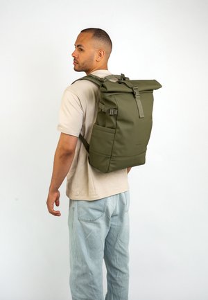 Zaino a rotolo verde realizzato in materiale resistente, dotato di spallacci regolabili, una fibbia frontale e tasche laterali per lo stoccaggio.