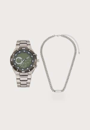 Montre en métal avec cadran vert et collier en maillons argentés. La montre présente des détails de chronographe et une finition polie.