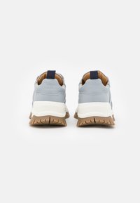 Světlomodré tenisky s texturovaným povrchem, bílé mezipodešve a hnědé gumové podešvi. Mají námořnickou poutko a kontrastní akcenty.