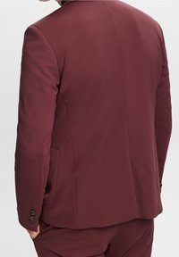 Burgundowa marynarka w garniturze, dopasowany krój, o gładkiej fakturze, z pojedynczym rozcięciem z tyłu i trzema guzikami na mankietach. Minimalistyczny design.