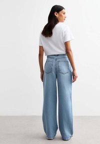 Light blue wide-leg jeans with a high waist, two back pockets, and visible stitching details, paired with a plain white t-shirt.