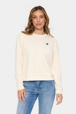 Beige Langarm-Sweatshirt mit rundem Ausschnitt, gerippten Bündchen und kleinem grünen Herz-Logo auf der linken Brust. Weicher Stoff, lockere Passform.