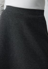 Gonna nera, elastica a forma di A con una trama liscia e una vita elasticizzata. Sottile motivo melange con un design che arriva fino al ginocchio.