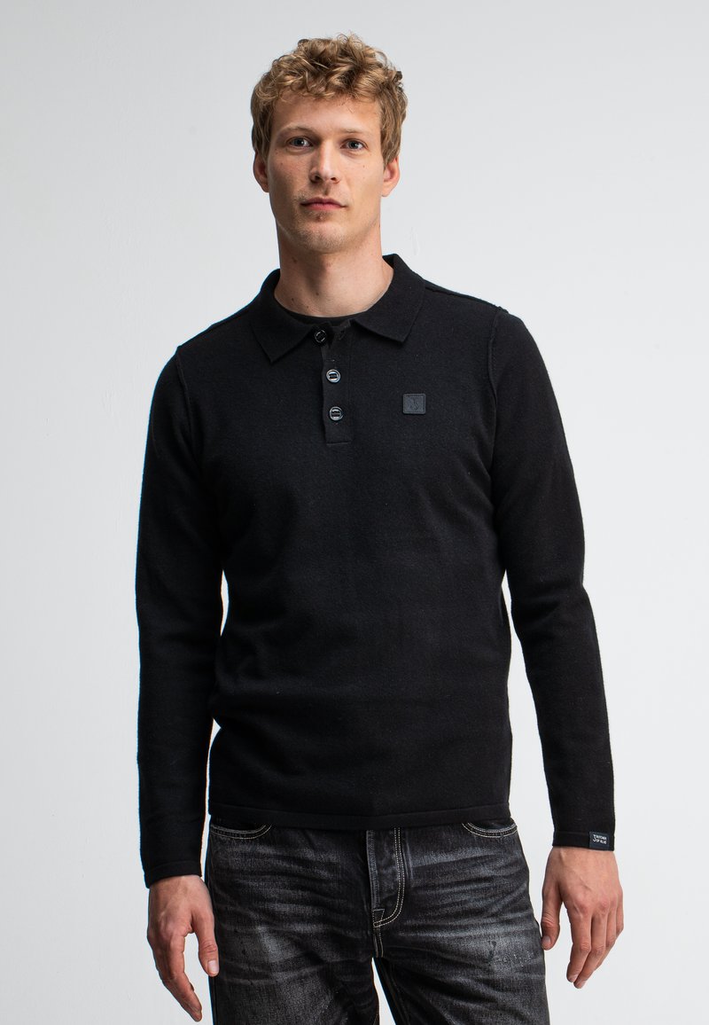 Schwarzes Longsleeve-Polohemd mit Kragen, Drei-Knopf-Leiste und einem dezenten Logo-Patch. Getragen mit dunklen Jeans aus Denim, glatte Textur.