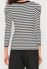 Schwarz-weißer gestreifter Ripp-Top mit dreiviertellangen Puffärmeln und Rundhalsausschnitt. Glatte Textur, figurbetonte Silhouette und kontrastierende Streifen.