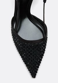 Czarne sandały na wysokim obcasie z wysmuklonym noskiem, teksturowaną tkaniną z diamentowym wzorem i regulowanymi paskami na kostce.