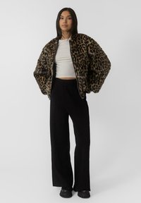 Jakna od umjetnog krzna s leopardovim uzorkom i oversized rukavima, kontrastni obični bijeli krojeni top i crne široke hlače. Crne platforme čizme.