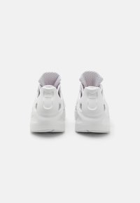 Vita atletiska skor med en slank design, andningsbar meshfoder och en texturerad gummisula. Bakifrån visas en vadderad krage och logotypdetalj.