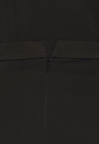 Närbild av en svart dragkedja som stänger baksidan av ett plagg gjort av mjuk, mörk tyg.