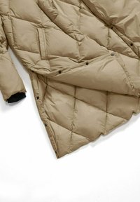 Giacca puffer beige con motivo a rombi, con polsini neri, bottoni a pressione e una tasca laterale all'orlo aperto.
