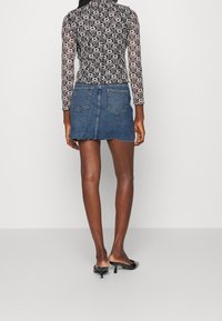Top a maniche lunghe con motivo bianco e nero abbinato a una mini gonna in denim blu con orlo sfrangiato e tasche posteriori. Muli neri con tacco completano il look.