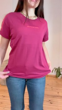 Fuchsia short-sleeve t-shirt with "COLOURFUL REBEL" text, made of soft fabric, relaxed fit, paired with blue jeans, displayed indoors.