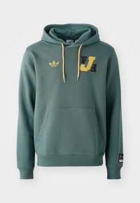 Grön hoodie av mjukt tyg, med en känguruficka, gula snoddar och tryckta svarta och gula logotyper på framsidan.