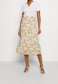 Kukallinen midihame, jossa vaalea tausta ja vaaleanpunaisia sekä vihreitä kukkia, liehuva helma ja istuva vyötärö. Yhdistetty valkoiseen toppiin ja sandaaleihin.