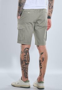 Green cargo shorts with multiple pockets, made of cotton-blend fabric, featuring a straight cut and smooth texture. Worn with white sneakers.