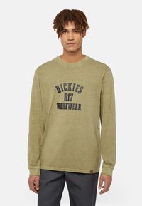 Olive green long-sleeve shirt with round neck, featuring "DICKIES 817 WORKWEAR" printed in dark navy. Relaxed fit and textured fabric.