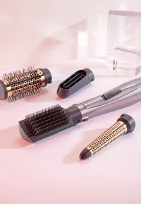 Strumenti per acconciare i capelli, tra cui una spazzola con setole in plastica, un cilindro oro e nero, e un'impugnatura grigia elegante con comandi. Visibili più attacchi.
