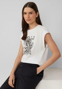 Witte katoenen t-shirt met zwart en beige grafische tekstontwerp. Korte capmouwen en een relaxte pasvorm, gecombineerd met donkere broeken. Eenvoudige textuur.