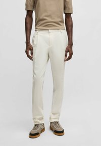 Pantaloni bianchi su misura in tessuto testurizzato, con una linea dritta e accentuati da sneakers beige. Abbinati a un top neutro.