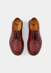 Bordeaux leren schoenen met zwarte veters, rond neuzen ontwerp, gele stiksels langs de zool, en geperforeerde binnenzool voor ademend vermogen.