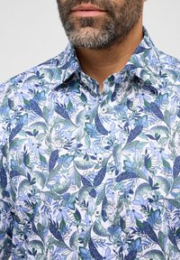 Camicia a maniche corte in cotone, con una fantasia botanica in blu chiaro e verde, dotata di bottoni e colletto classico.
