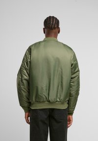 Giacca bomber verde in satin con polsini e vita a coste; presenta maniche imbottite e una superficie liscia e lucida.