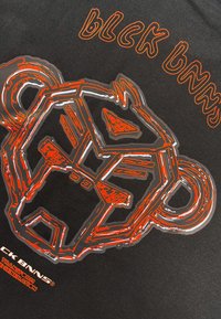 Zwarte stoffen T-shirt met een oranje omlijnde graphic van een gestileerd dierengezicht en de tekst "blck bnns" in een vet, modern lettertype.
