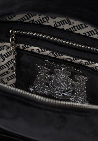 Črna semiš torbica z notranjostjo, ki vključuje srebrni emblem 'Juicy Couture' in žep na zadrgo, obogaten s vzorčasto kremno tkanino.