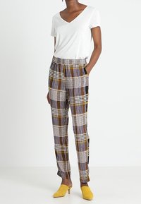 Vit t-shirt med V-ringning, ihopparad med mönstrade avsmalnande byxor i kräm, gult, lila och svart. Suede gula klackar fulländar outfiten.