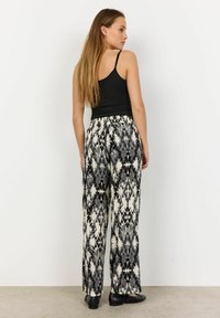 Pantaloni a gamba larga con un motivo astratto in bianco e nero, vita elastica e tessuto fluido. Abbinati a un top aderente nero e ballerine.